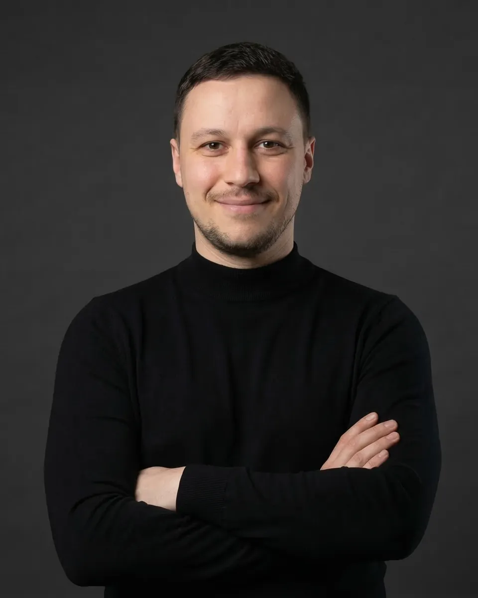 Karol Ostasz w czarnym golfie, z założonymi rękami, uśmiechnięty